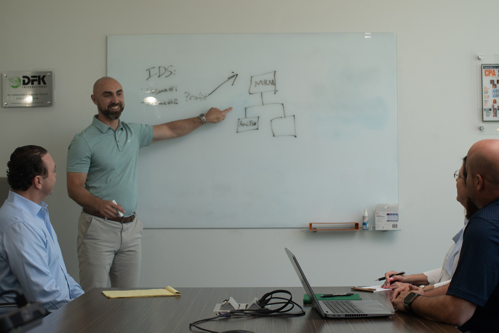 Man points at a white board while smiling